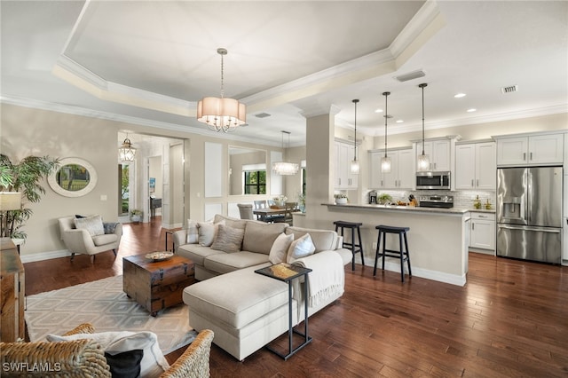 living room with a chandelier, dark hardwood / wood-style floors, a tray ceiling, and crown molding