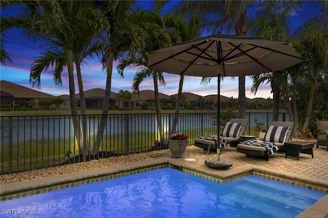 pool at dusk with a patio area and a water view