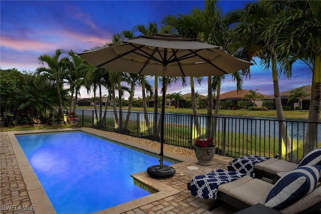 pool at dusk with a water view and a patio