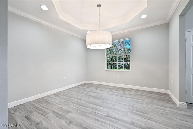 empty room featuring light hardwood / wood-style floors, a raised ceiling, and crown molding