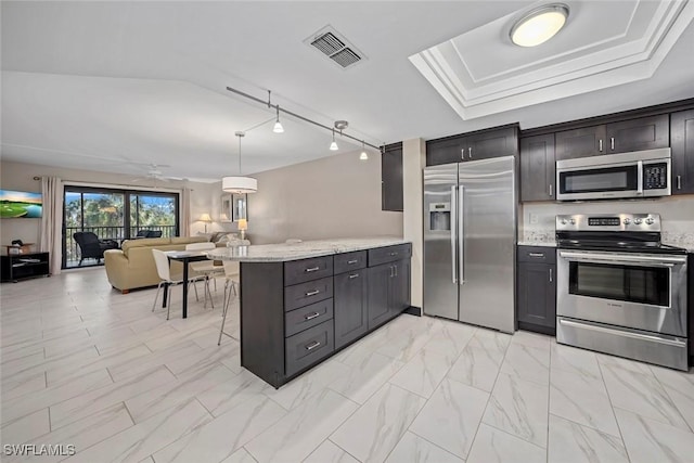 kitchen featuring a breakfast bar, stainless steel appliances, light stone counters, a tray ceiling, and kitchen peninsula