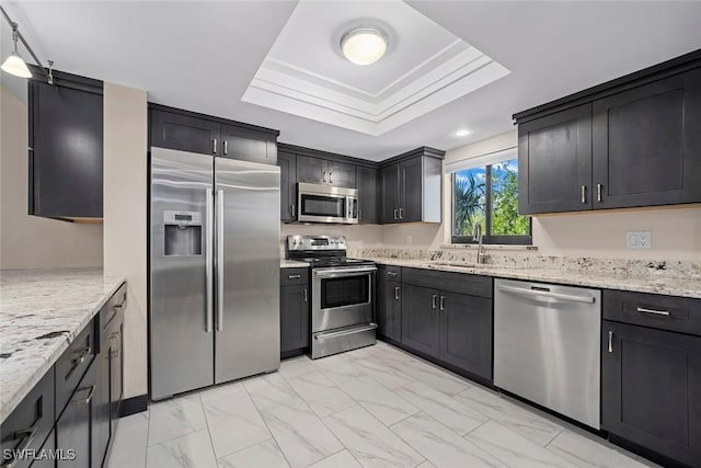 kitchen featuring light stone counters, sink, stainless steel appliances, and a raised ceiling