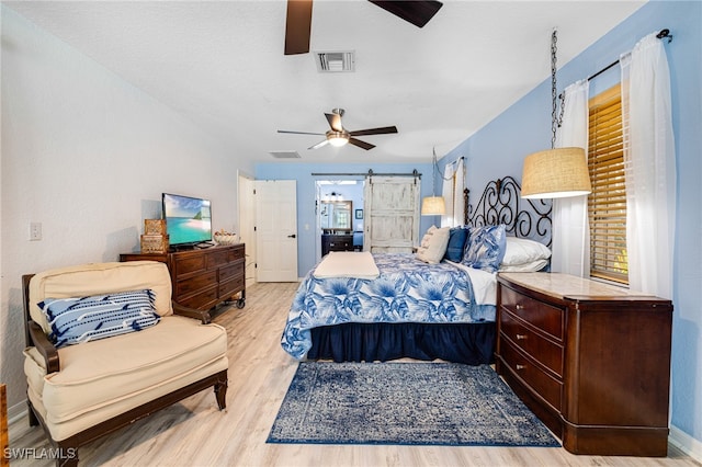 bedroom with ceiling fan, a barn door, light hardwood / wood-style floors, and multiple windows