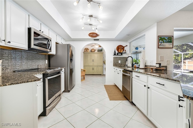 kitchen with tasteful backsplash, stainless steel appliances, a raised ceiling, dark stone countertops, and white cabinetry