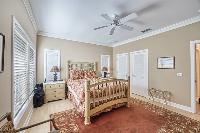 bedroom with ornamental molding, two closets, ceiling fan, light hardwood / wood-style flooring, and multiple windows