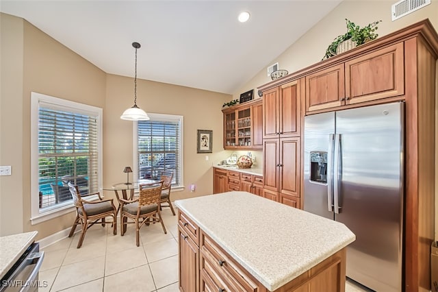 kitchen with pendant lighting, a center island, vaulted ceiling, light tile patterned floors, and appliances with stainless steel finishes