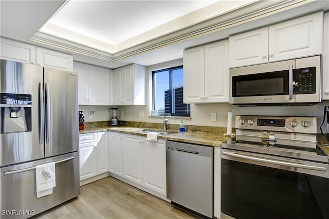 kitchen featuring white cabinets, a raised ceiling, light hardwood / wood-style flooring, light stone counters, and stainless steel appliances