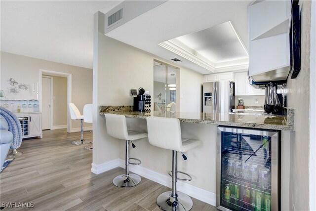 kitchen with white cabinetry, beverage cooler, a kitchen breakfast bar, stainless steel fridge with ice dispenser, and light hardwood / wood-style floors