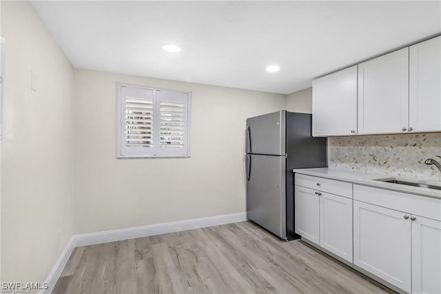 kitchen with backsplash, white cabinets, sink, light hardwood / wood-style flooring, and stainless steel refrigerator