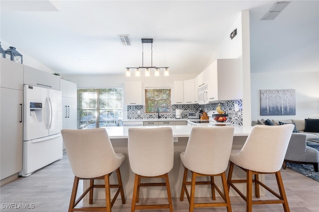 kitchen with light wood-type flooring, tasteful backsplash, white appliances, decorative light fixtures, and a breakfast bar area