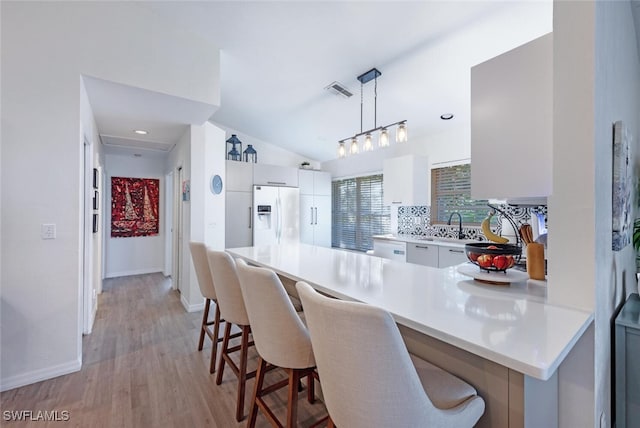 kitchen with a breakfast bar, white appliances, white cabinets, hanging light fixtures, and tasteful backsplash