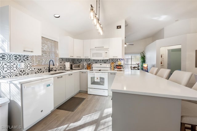 kitchen with sink, a kitchen bar, white appliances, and hanging light fixtures