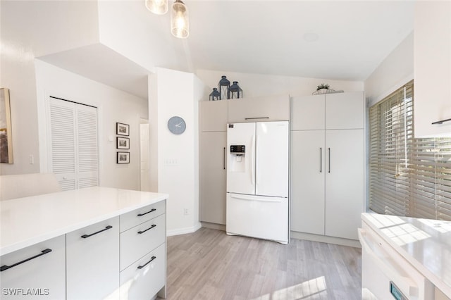 kitchen with white cabinetry, white fridge with ice dispenser, hanging light fixtures, light hardwood / wood-style floors, and vaulted ceiling