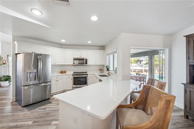 kitchen with sink, light hardwood / wood-style flooring, kitchen peninsula, stainless steel appliances, and white cabinets