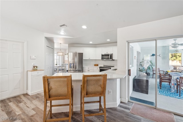 kitchen featuring white cabinets, a kitchen breakfast bar, kitchen peninsula, stainless steel appliances, and light hardwood / wood-style flooring