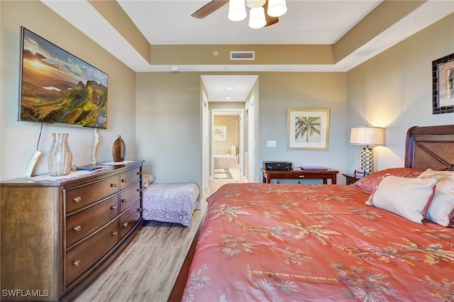 bedroom featuring ensuite bathroom, hardwood / wood-style floors, and a tray ceiling