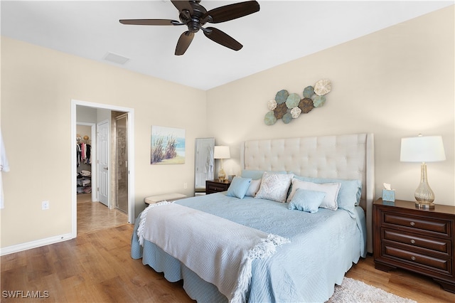 bedroom featuring a spacious closet, a closet, light hardwood / wood-style flooring, and ceiling fan