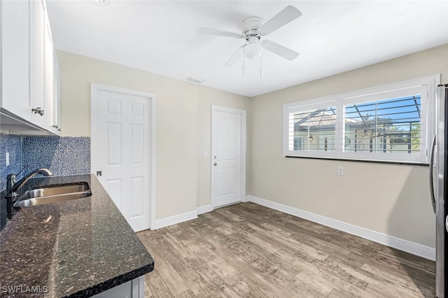 kitchen featuring sink, dark stone counters, decorative backsplash, white cabinets, and light wood-type flooring