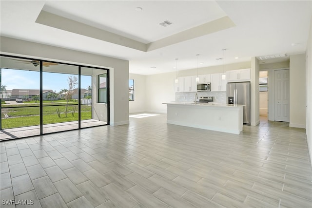 unfurnished living room with a tray ceiling, ceiling fan, and light wood-type flooring