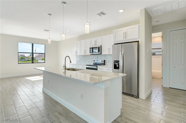 kitchen featuring white cabinetry, sink, stainless steel appliances, pendant lighting, and a kitchen island with sink