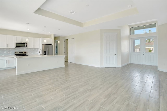 unfurnished living room with a raised ceiling, light hardwood / wood-style flooring, and french doors