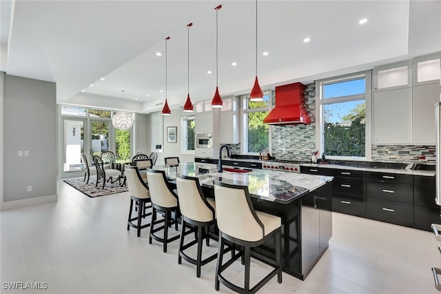 kitchen with backsplash, premium range hood, a healthy amount of sunlight, white cabinets, and a large island