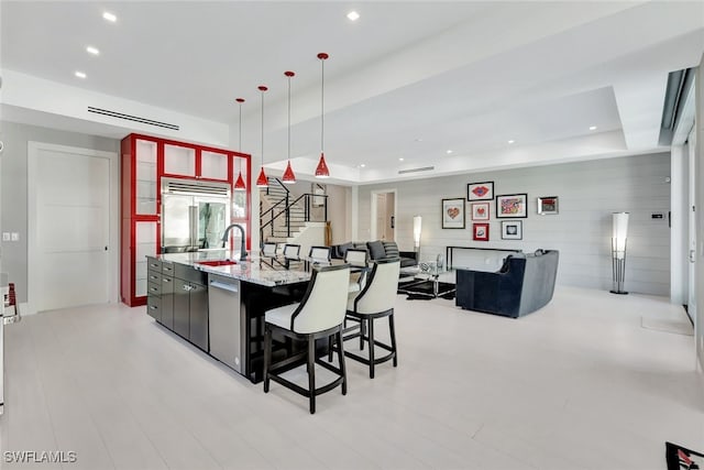 kitchen featuring a large island with sink, sink, appliances with stainless steel finishes, a tray ceiling, and decorative light fixtures