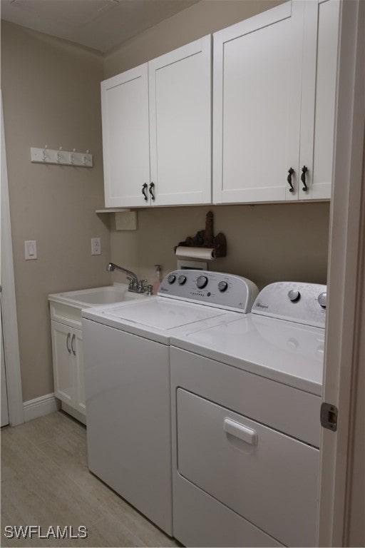 laundry room featuring washer and clothes dryer, cabinets, sink, and light hardwood / wood-style flooring