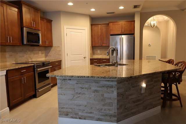 kitchen with stone counters, sink, stainless steel appliances, a kitchen breakfast bar, and a center island with sink