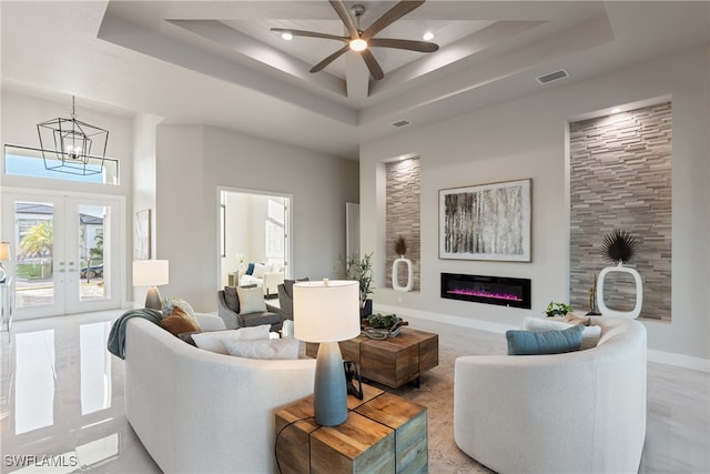 living room featuring french doors, a raised ceiling, ceiling fan with notable chandelier, and a high ceiling