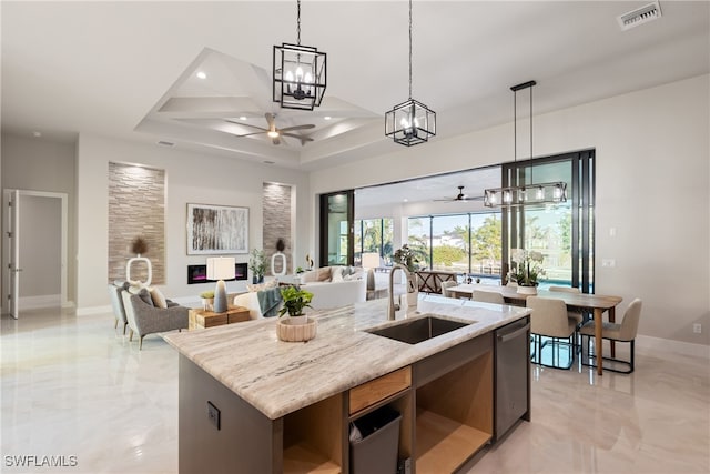 kitchen featuring sink, dishwasher, hanging light fixtures, light stone counters, and a center island with sink