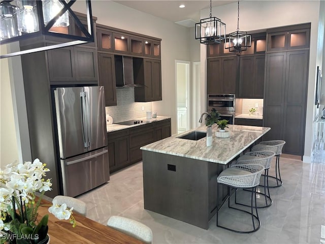 kitchen featuring wall chimney exhaust hood, sink, light stone counters, stainless steel appliances, and a kitchen island with sink