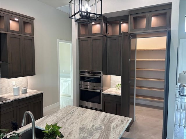 kitchen featuring light stone counters, tasteful backsplash, decorative light fixtures, dark brown cabinets, and stainless steel double oven