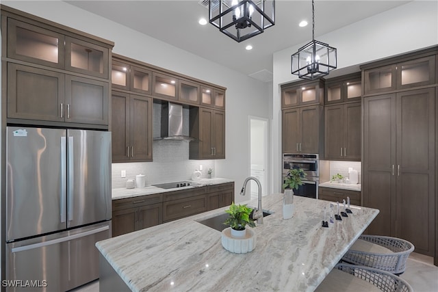 kitchen with light stone countertops, appliances with stainless steel finishes, a kitchen island with sink, and wall chimney exhaust hood