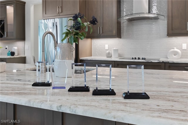 kitchen featuring dark brown cabinetry, wall chimney range hood, light stone counters, and black electric cooktop