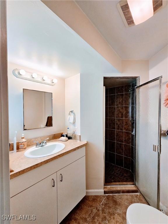 bathroom with tile patterned flooring, vanity, toilet, and walk in shower