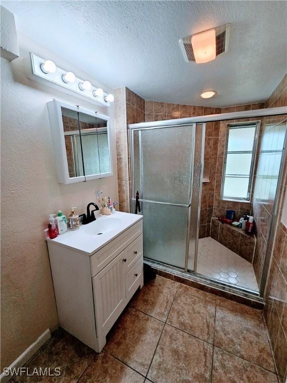 bathroom with tile patterned floors, vanity, an enclosed shower, and a textured ceiling