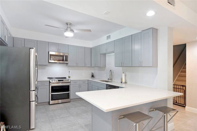 kitchen with sink, ceiling fan, appliances with stainless steel finishes, a kitchen bar, and kitchen peninsula