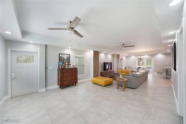 living room featuring ceiling fan with notable chandelier and a tray ceiling