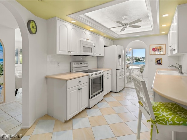 kitchen featuring a raised ceiling, sink, white cabinets, and white appliances