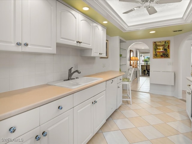 kitchen with a raised ceiling, sink, ceiling fan, tasteful backsplash, and white cabinetry