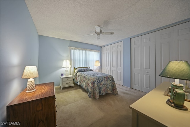 carpeted bedroom with a textured ceiling, two closets, and ceiling fan