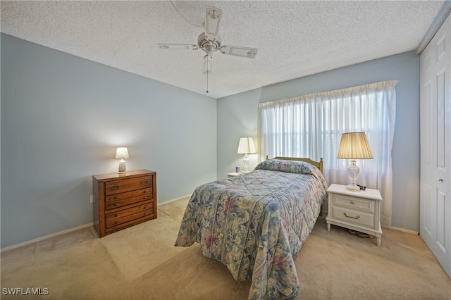 bedroom featuring ceiling fan, a closet, light colored carpet, and a textured ceiling