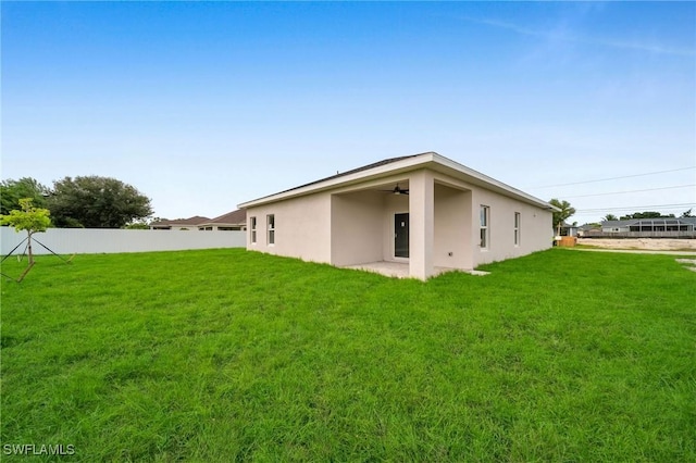 rear view of property with fence, stucco siding, a lawn, and ceiling fan