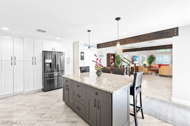 kitchen with a kitchen bar, stainless steel fridge, pendant lighting, white cabinets, and a kitchen island