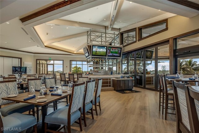 dining area featuring bar, crown molding, a towering ceiling, and light wood-type flooring