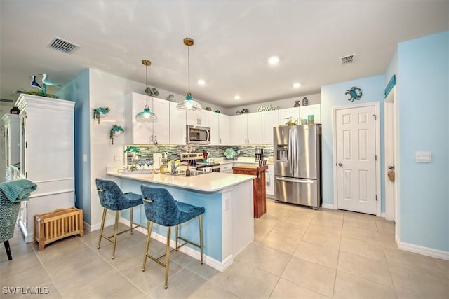 kitchen with tasteful backsplash, kitchen peninsula, pendant lighting, white cabinets, and appliances with stainless steel finishes