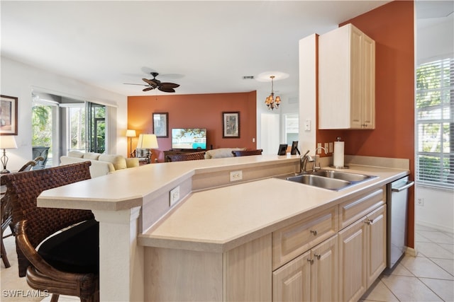 kitchen featuring a breakfast bar, ceiling fan with notable chandelier, sink, stainless steel dishwasher, and light tile patterned flooring