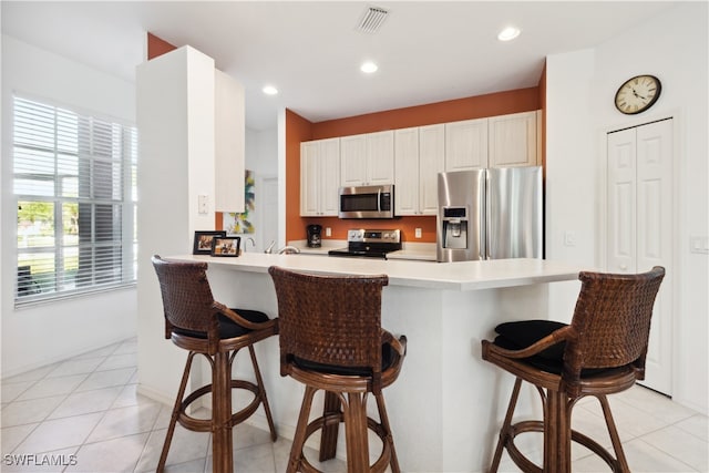 kitchen with a kitchen breakfast bar, kitchen peninsula, light tile patterned flooring, and stainless steel appliances