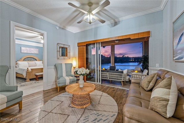 living room with ceiling fan, light hardwood / wood-style floors, a textured ceiling, a water view, and ornamental molding